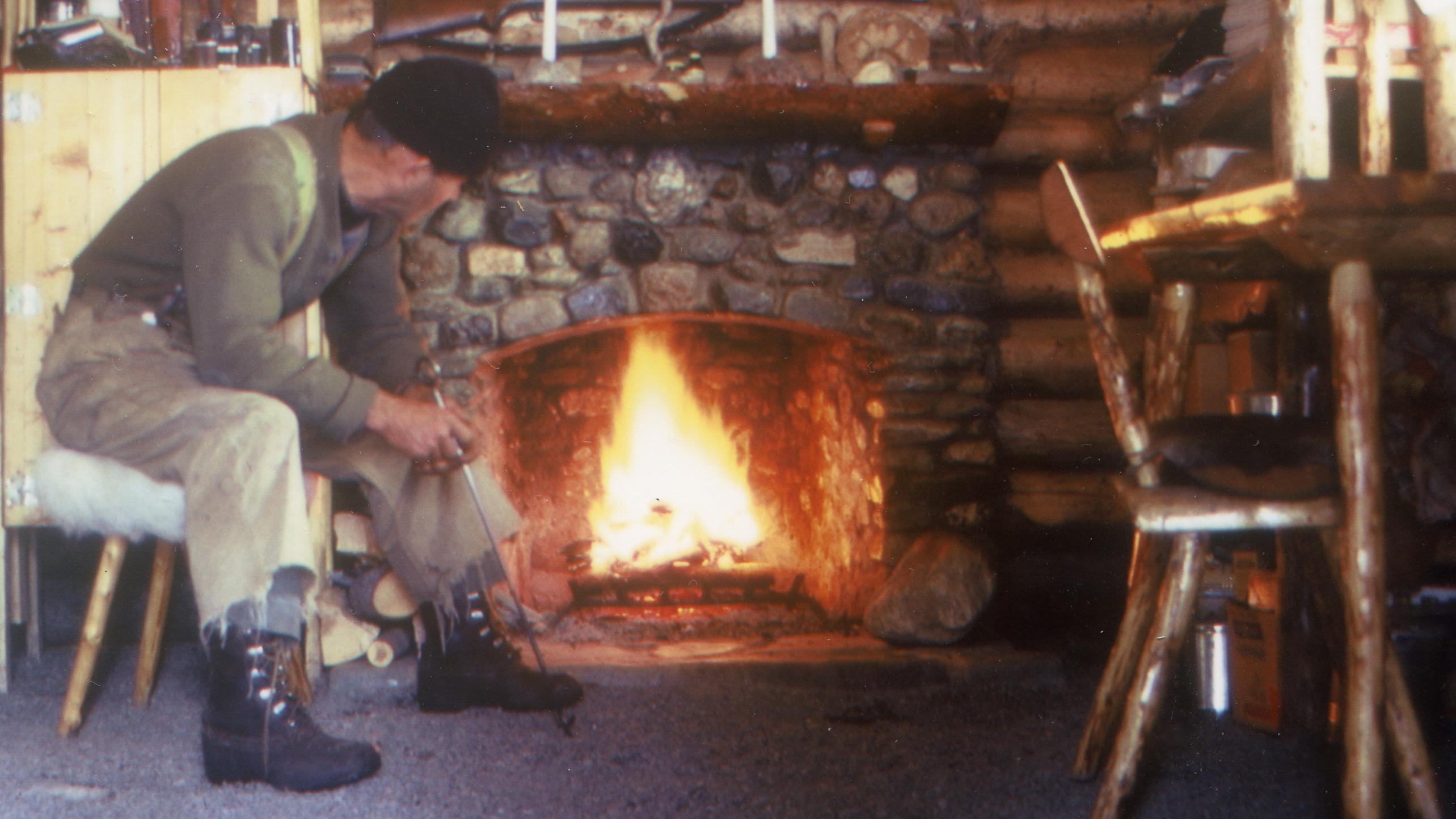 Image of a man in front of a fireplace in a log cabin.