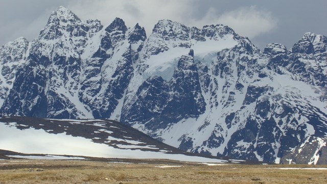 Image of a high, snow covered mountain range with clouds in the background.