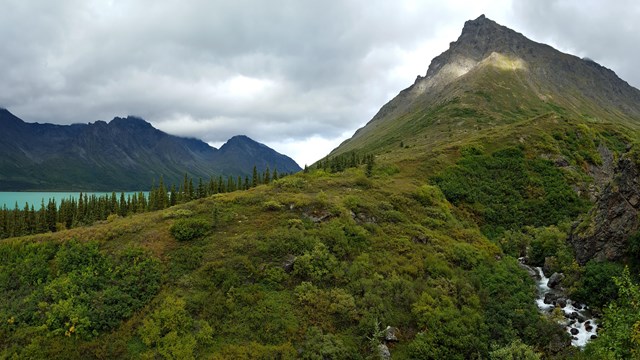 Image of creek flowing through valley with tall mountains in the background.