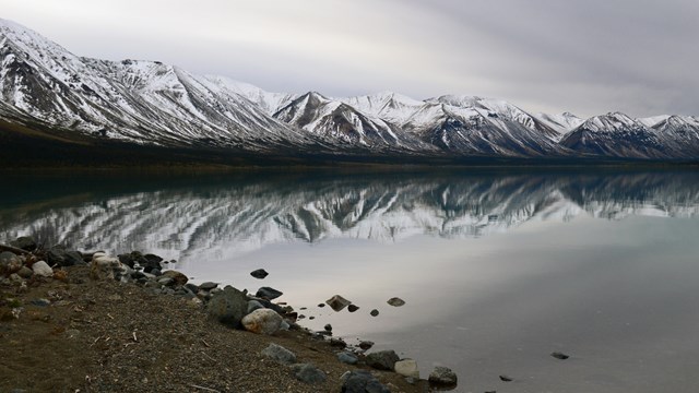 Image of snow capped mountains with lake shore in foreground.