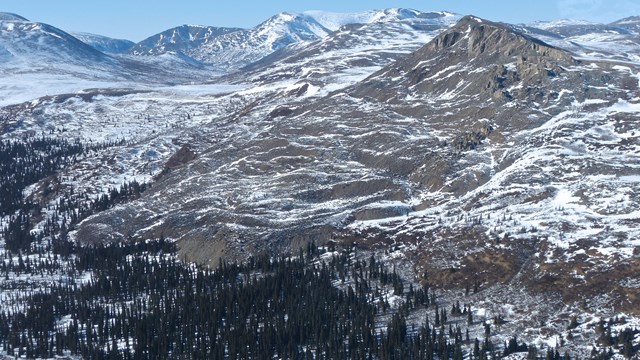 A brown mountainous landscape with patches of snow beneath blue skies