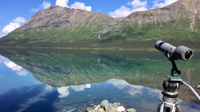 a spotting scope pointed at a mountain that is reflecting in a lake