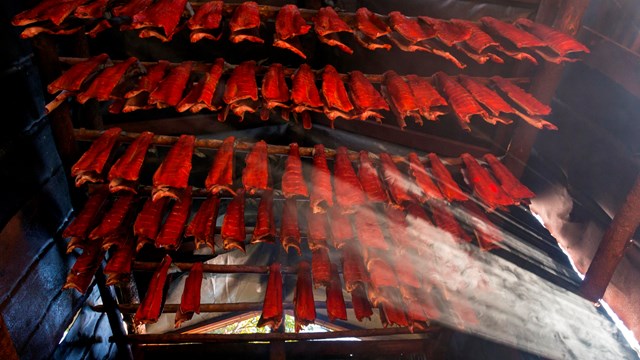 Photo of many fillets of red salmon hanging on a wooden rack to dry intdoors.
