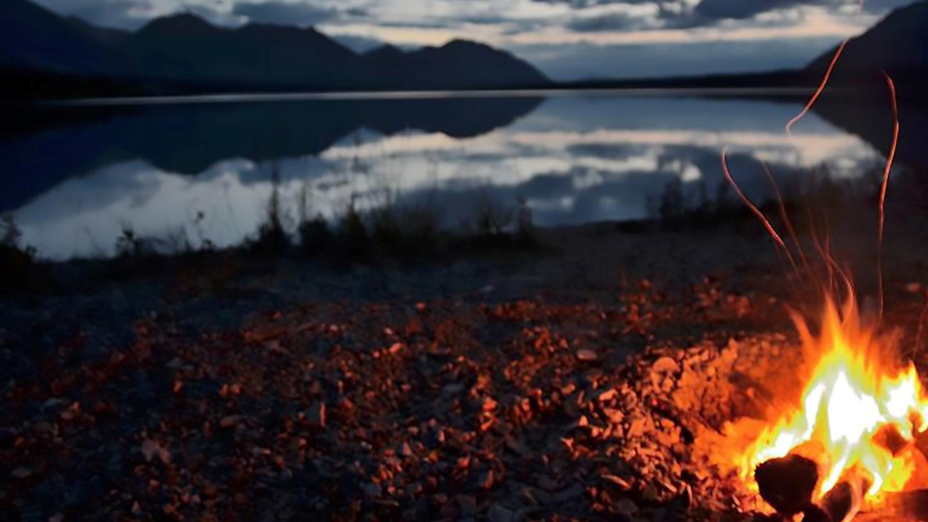 Photo of a campfire near a lake at dusk.