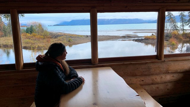 woman looking out window of cabin onto creek
