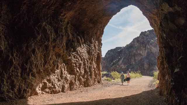 2 hikers enter a cone of light cast by the large opening of a tunnel on the Historic Railroad Trail.