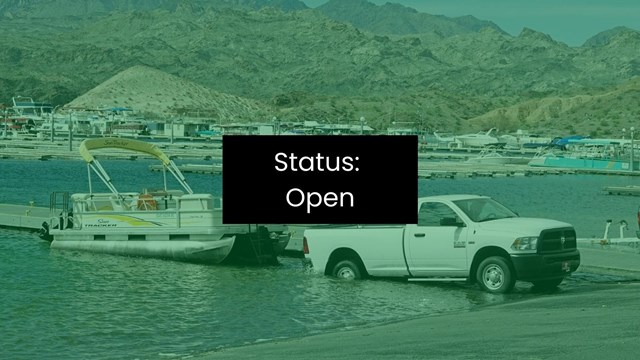 A truck launches a boat into an enclosed body of water with mountains in background.
