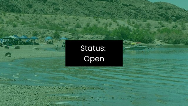 A beach sits along the shoreline of an enclosed lake with mountains in background.