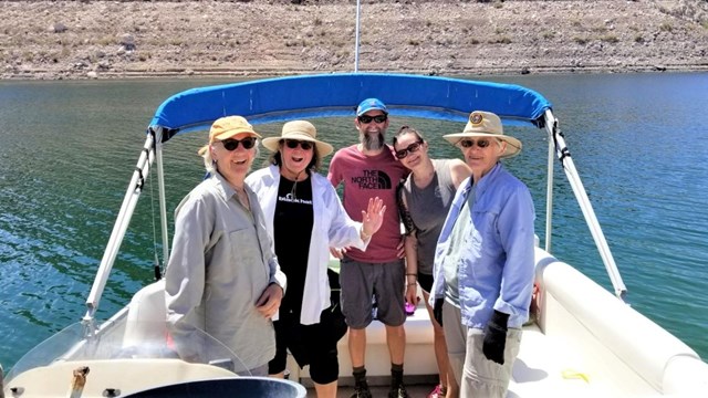 Five volunteers smile on a boat overlooking a lake.