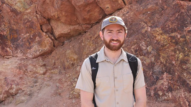 A volunteer smiles in front of a rocky, canyon.