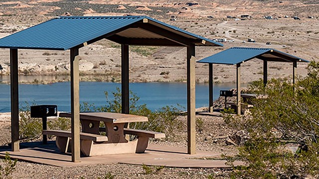Two picnic shelters with a large, enclosed body of water in the background.
