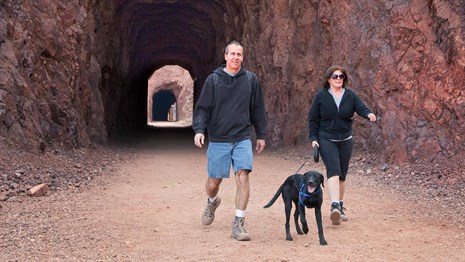 A man and a woman hiking and a trail with a dog. 