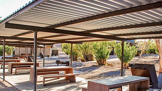 Several picnic tables sit under a shaded picnic shelter.