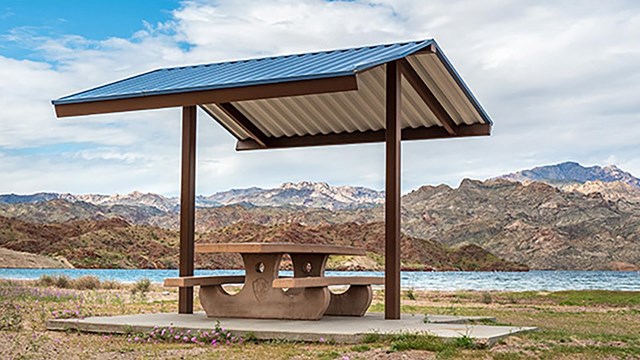 A table with a shade shelter overlooking a body of water.