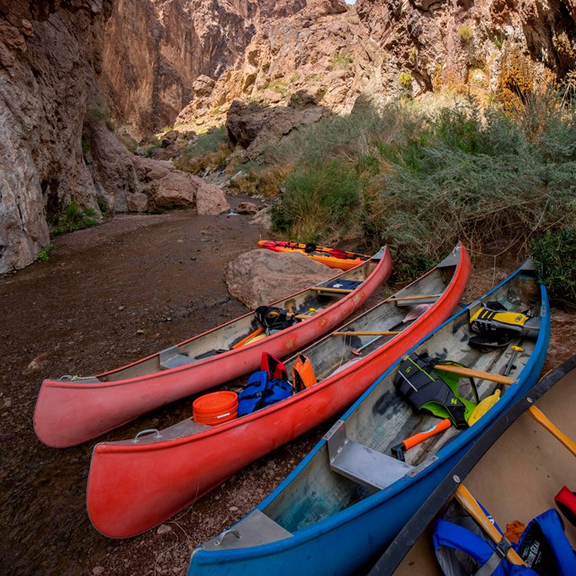 Three kayaks with no one in them on the side of a river.