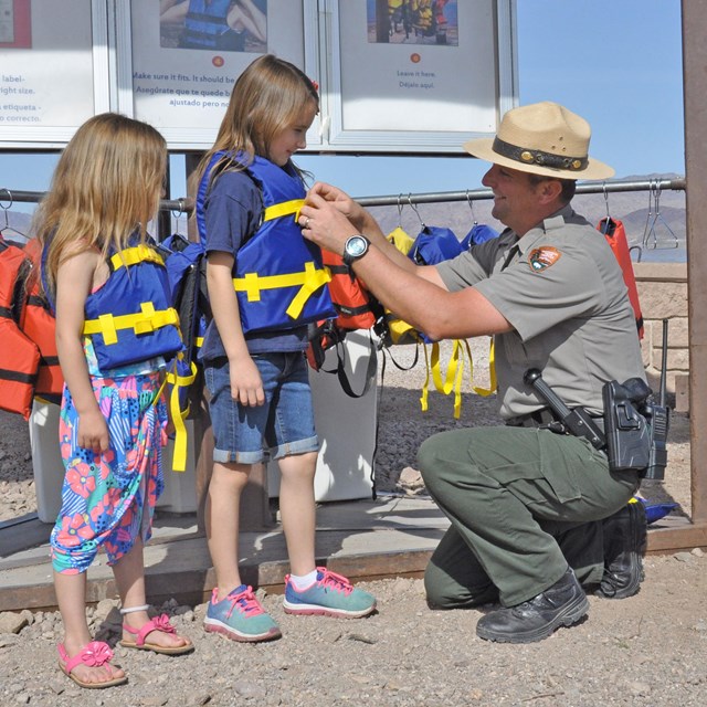 A ranger is putting life vests on two young girls.