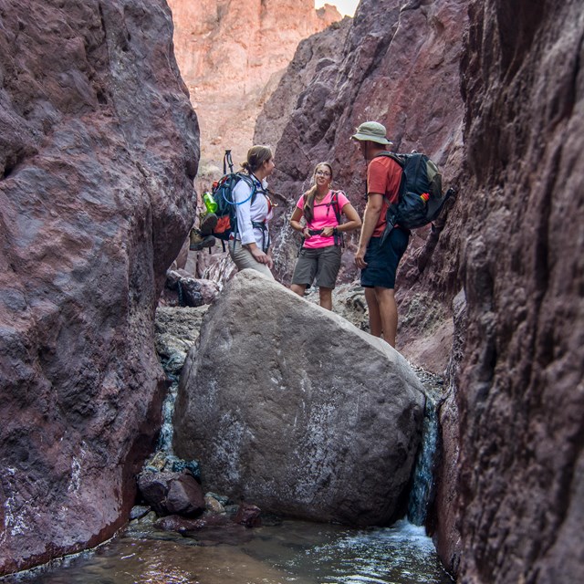 Three hikers walking through a slot canyon. 