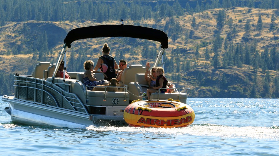 A family with a dog on a motorboat are waving as they cross the lake.