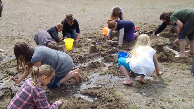 Students attempt to build features on a sandy beach that will withstand a massive flood.