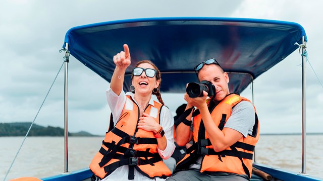 Two people enjoying a day on the lake, boating and taking pictures while wearing their PFDs.