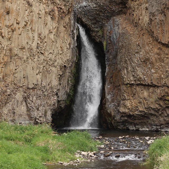 a waterfall between lichen-covered rocks meets a shallow creek