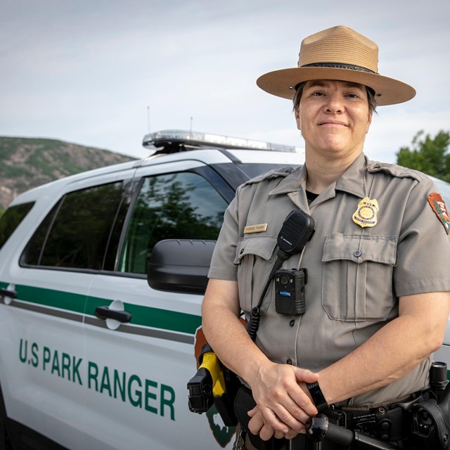 A visitor and resource protection ranger standing by a park vehicle.