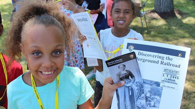 A young girl wears a plastic badge and holds up papers