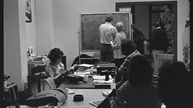 Latino community post-fieldwork workshop. 7 people in a classroom reading and working on projects.