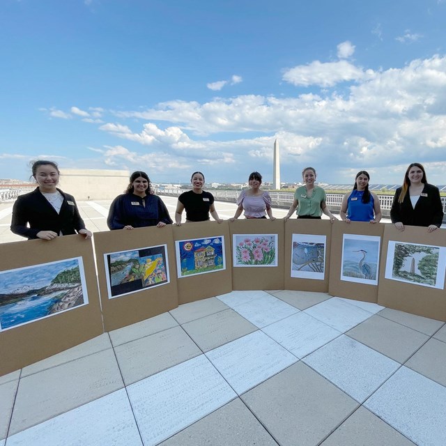 A group of interns holding up their artwork while standing on a rooftop