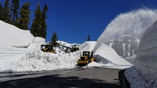 A bulldozer and rotary plow clear snow from a road