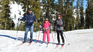 A man, woman, and girl pose for a photo on cross-country skis in a mountain landscape.