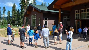 A group of people stand in a circle while conducting an activity outside of a wood building