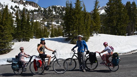 Two adults and two children on two extendable bicycles on a highway with snow in the background