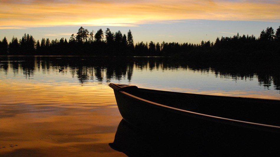 A canoe on a lake reflecting orange and yellow colors at sunset.