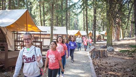 A group of young girls walk along a rock path past a line of canvas tents