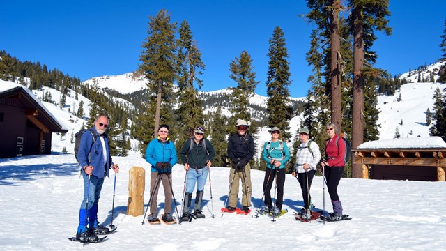 Four men and three women on showshoes backed by mountain peaks.