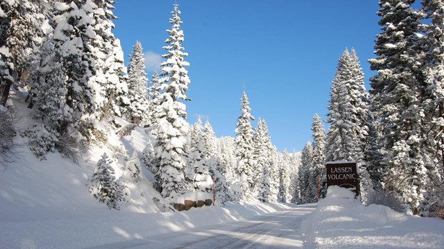 A brown sign reads "Lassen Volcanic" to the right of a snowy road.