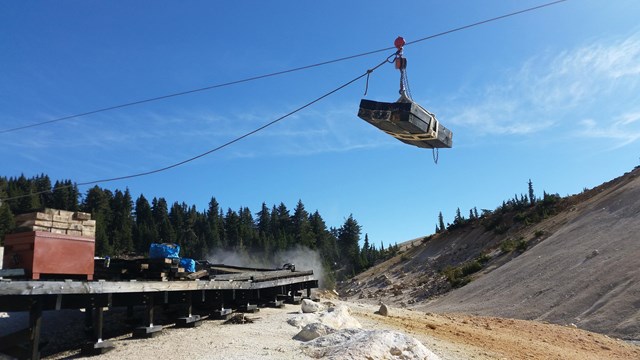 A load of lumber is transported by highline over a hydrothermal basin