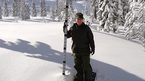 A woman in uniform stands on snowshoes next to a pole buried in snow