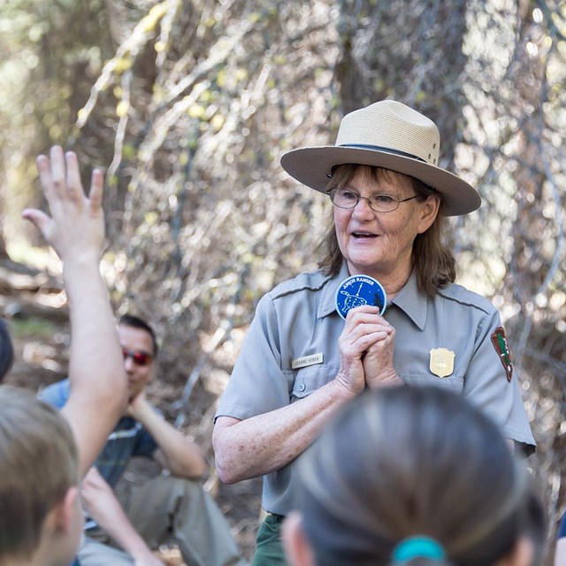 A female ranger holds a badge in front of a group of children.
