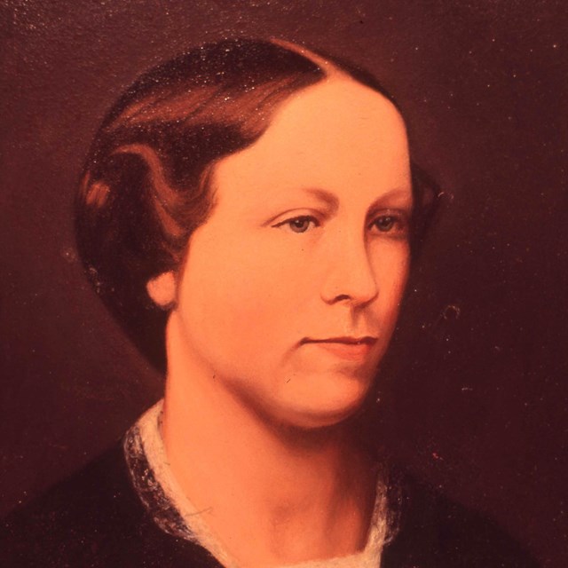 Portrait of a young woman with short hair and black top with a white, lace collar. 