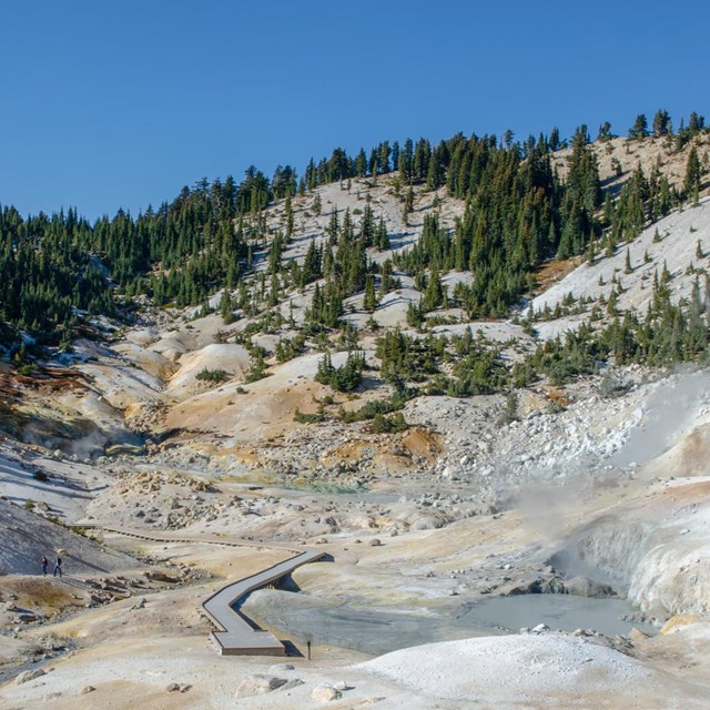 A barren basin with steam rising and boardwalk crossing through