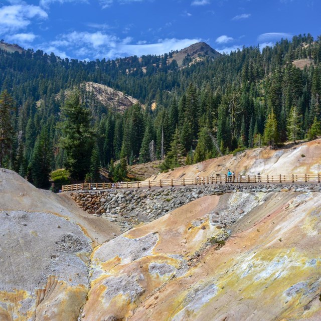 A barren hillside covered in bright white and yellow soils below a road with wooden guardrails