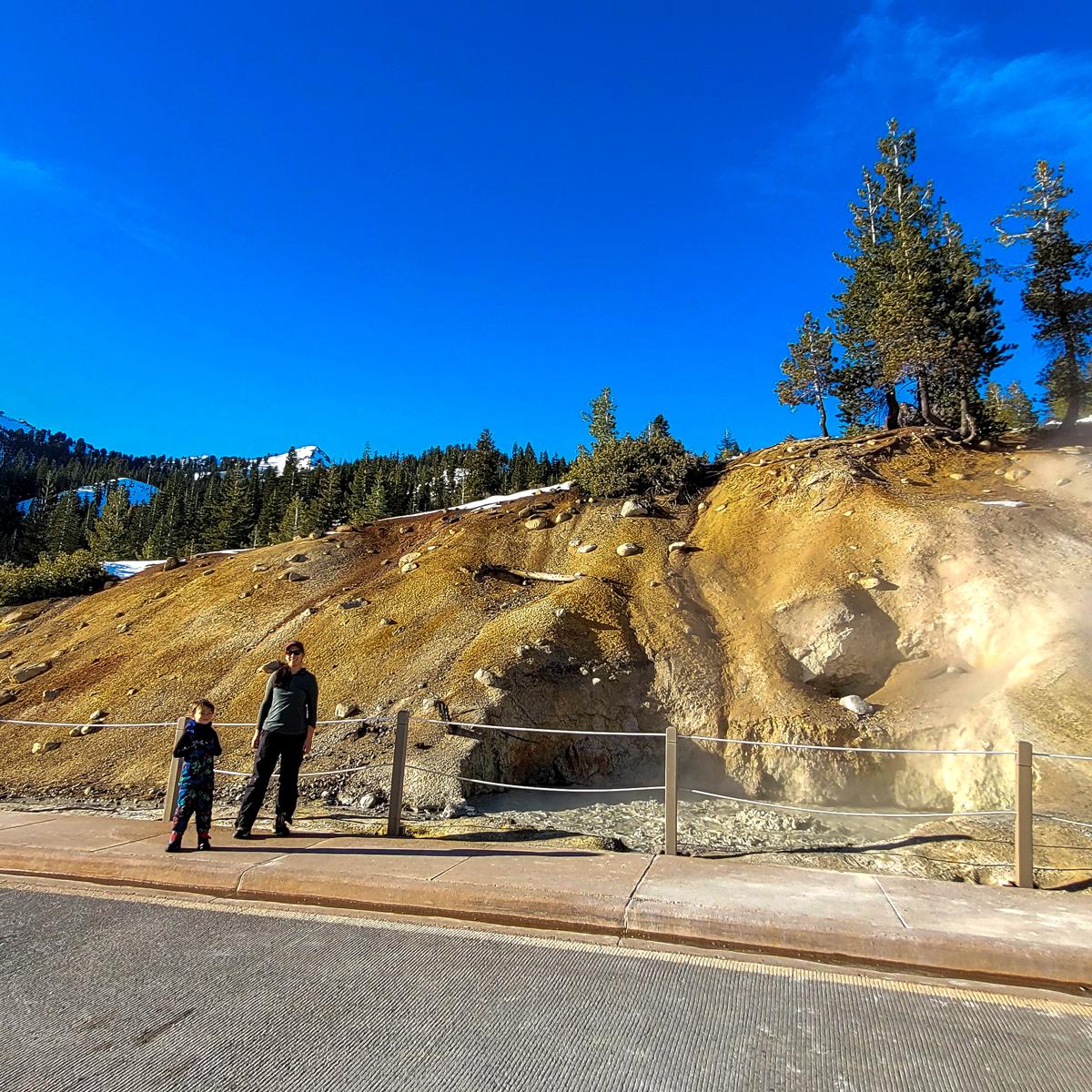 A woman and a young boy pose for a photo next to a boiling pool on the side of a road. 