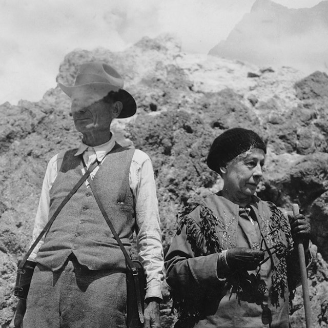 A black and white photo of a man and woman on the summit of a volcanic peak.