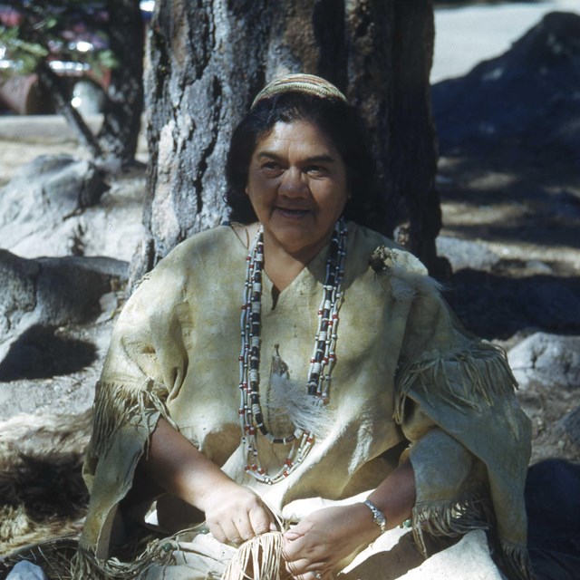 A women in traditional American Indian dress holding a woven basket