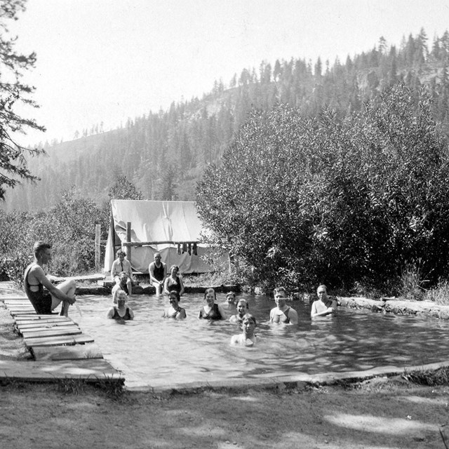 A group people in a rustic pool and another group standing to the right