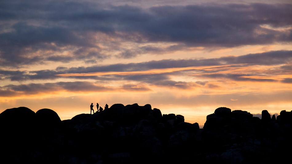 Silhouettes of people on rocky ridgeline at sunset