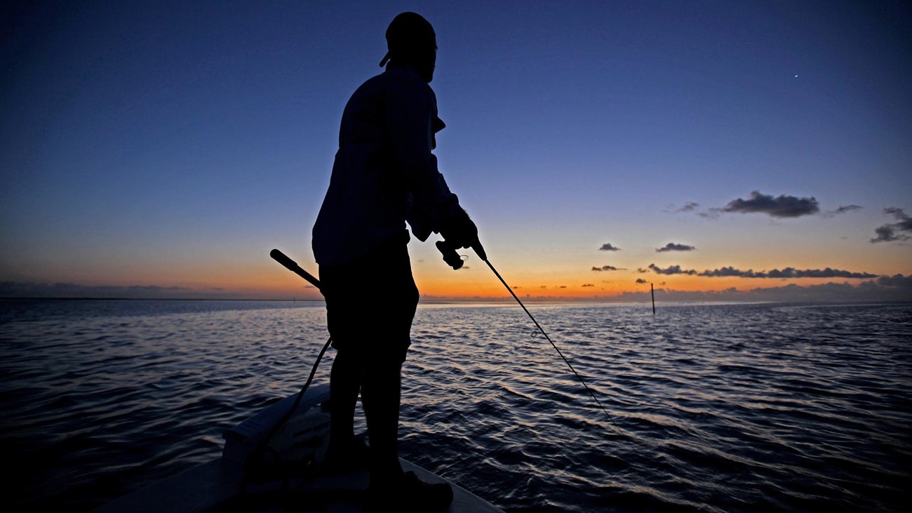 Silhouette of man fishing on flat ocean at sunrise