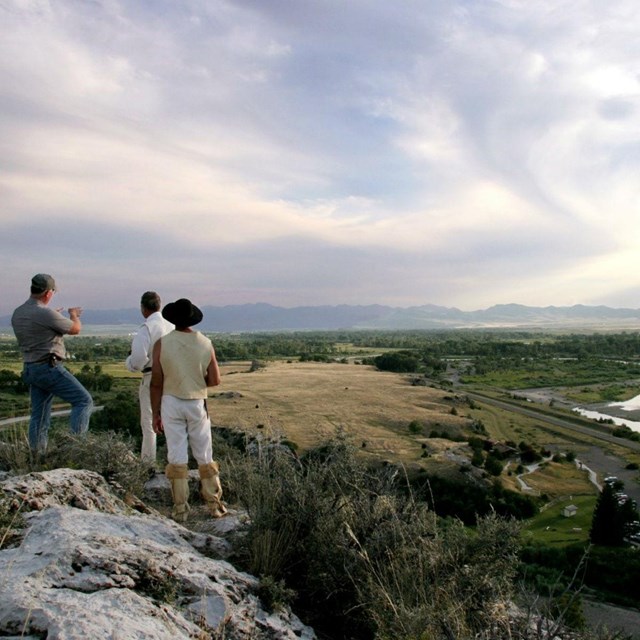 Three men standing on a rock overlooking valley.